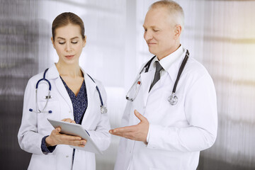 Elderly confident doctor and woman-physician discussing current disease therapy while standing in...
