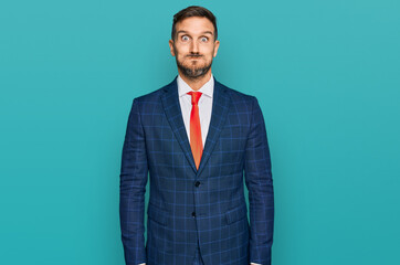 Handsome man with beard wearing business suit and tie puffing cheeks with funny face. mouth inflated with air, crazy expression.