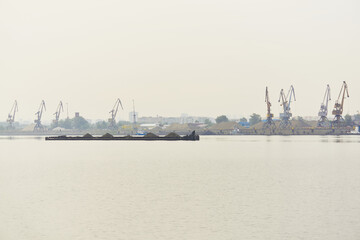industrial river waterscape with dry cargo barge and cargo terminal in morning fog