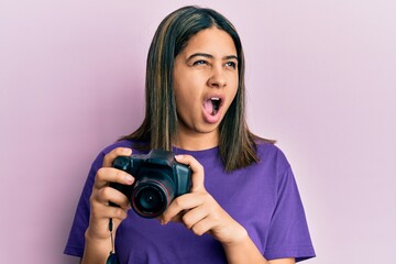 Young latin woman using reflex camera angry and mad screaming frustrated and furious, shouting with anger. rage and aggressive concept.