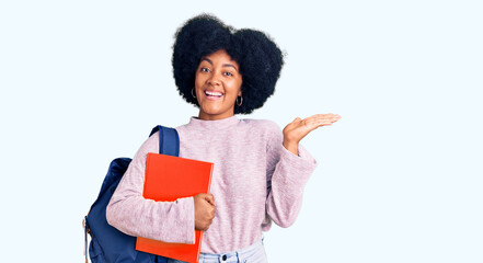 Young african american girl wearing student backpack holding book celebrating victory with happy smile and winner expression with raised hands