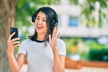 Young hispanic woman doing video call using smartphone and headphones at the city.