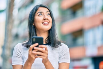 Young hispanic woman smiling happy using smartphone at the city.