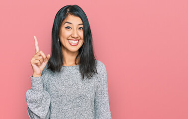 Beautiful asian young woman wearing casual clothes pointing finger up with successful idea. exited...