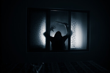 Silhouette of an unknown shadow figure on a door through a closed glass door. The silhouette of a human in front of a window at night.