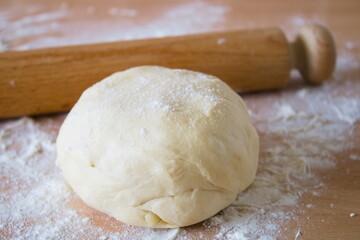 Ball of dough, pastry, on the wooden work top with scattered flour, rolling pin in the background