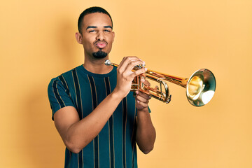 Young african american man playing trumpet looking at the camera blowing a kiss being lovely and...