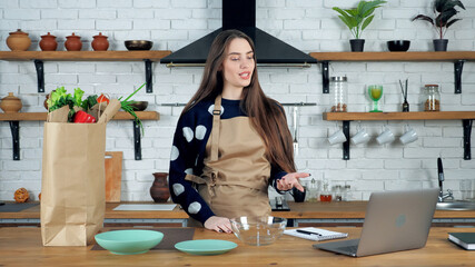 Beautiful woman housewife in beige apron talking teacher studying online remote video call conference webcam laptop computer, distance education learning chef cook culinary course in home kitchen