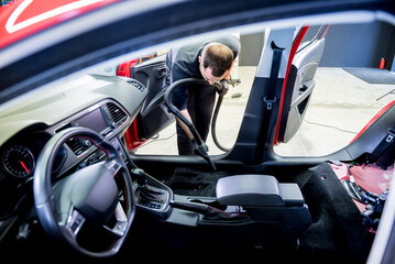 Car service worker cleaning car interior with a vacuum cleaner