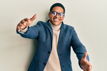 Naklejka premium Young handsome hispanic man wearing elegant clothes and glasses looking at the camera smiling with open arms for hug. cheerful expression embracing happiness.