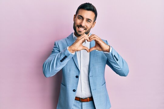 Young hispanic businessman wearing business jacket smiling in love doing heart symbol shape with hands. romantic concept.