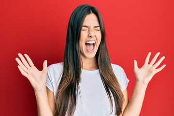 Young brunette woman wearing casual white tshirt over red background celebrating mad and crazy for...