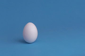 A white egg on a blue background. The concept of minimalism. Side view. A card with a copy of the place for the text.
