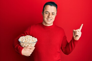 Handsome young man eating popcorn smiling happy pointing with hand and finger to the side