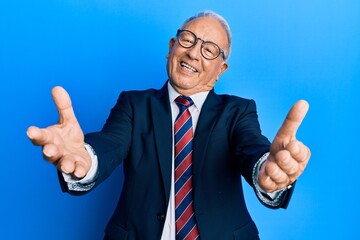 Senior caucasian man wearing business suit and tie looking at the camera smiling with open arms for hug. cheerful expression embracing happiness. - obrazy, fototapety, plakaty