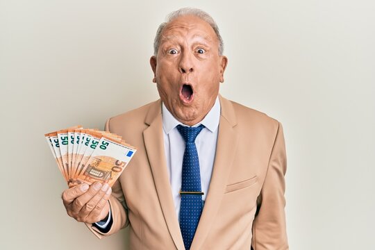 Senior caucasian man holding euro banknotes scared and amazed with open mouth for surprise, disbelief face