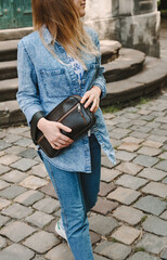 Girl in a denim suit and a dark brown handbag walks around the city.