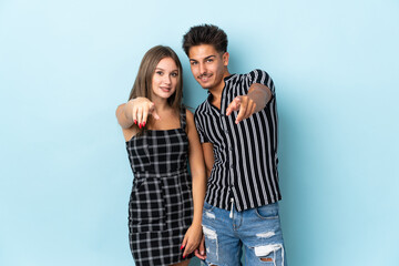 Teenager caucasian couple isolated on blue background points finger at you with a confident expression