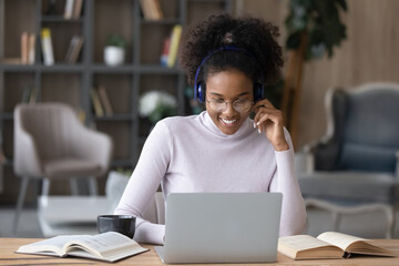 Smiling African American woman in earphones look at laptop talk online on video call on gadget....