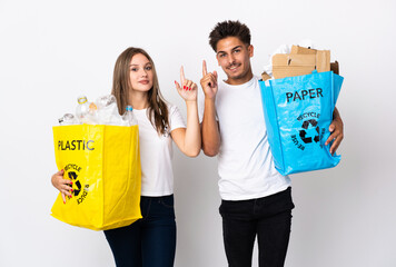 Young couple holding a bag full of plastic and paper isolated on white background pointing up a great idea