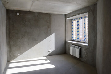 A room in a rough finish with a window and a radiator in a new building