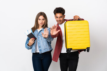 Traveler couple holding a suitcase isolated on blue background making stop gesture denying a...