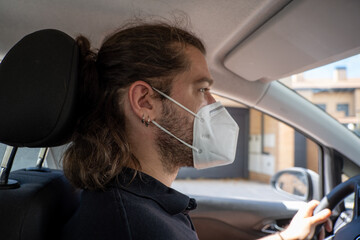 Young guy with long hair wearing a face mask by COVID-19 driving