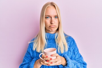 Young blonde girl wearing winter sweater and drinking a cup of hot coffee depressed and worry for distress, crying angry and afraid. sad expression.