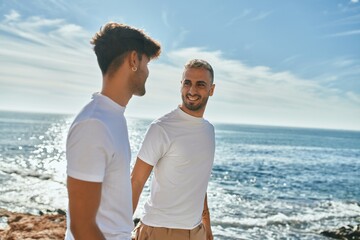 Young gay couple smiling happy walking at the beach promenade.