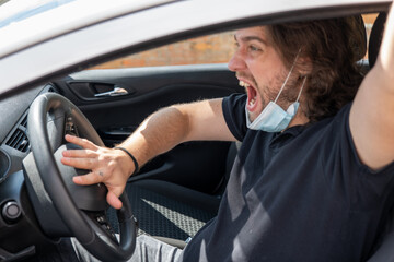 Young guy with long hair wearing a mask by COVID-19 driving in anger