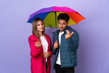 Couple holding an umbrella isolated on blue background inviting to come with hand. Happy that you came