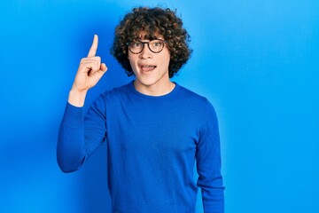 Handsome young man wearing casual clothes and glasses pointing finger up with successful idea....
