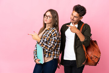 Young student couple isolated on white background pointing finger to the side in lateral position