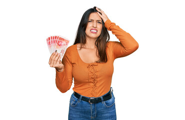 Beautiful hispanic woman holding 20 israel shekels banknotes stressed and frustrated with hand on head, surprised and angry face