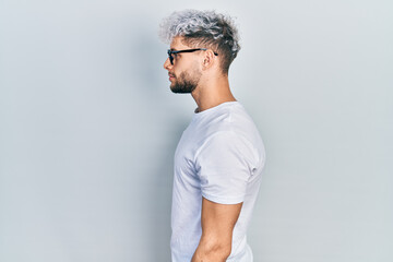 Young hispanic man with modern dyed hair wearing white t shirt and glasses looking to side, relax profile pose with natural face and confident smile.