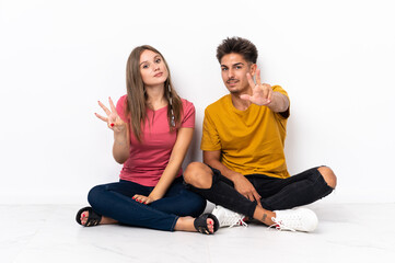 Fototapeta na wymiar Young couple sitting on the floor isolated on white background happy and counting three with fingers