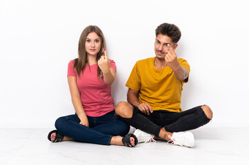 Fototapeta na wymiar Young couple sitting on the floor isolated on white background doing coming gesture