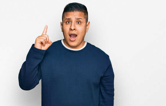 Young latin man wearing casual clothes pointing finger up with successful idea. exited and happy. number one.