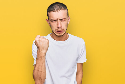 Hispanic young man wearing casual white t shirt angry and mad raising fist frustrated and furious while shouting with anger. rage and aggressive concept.