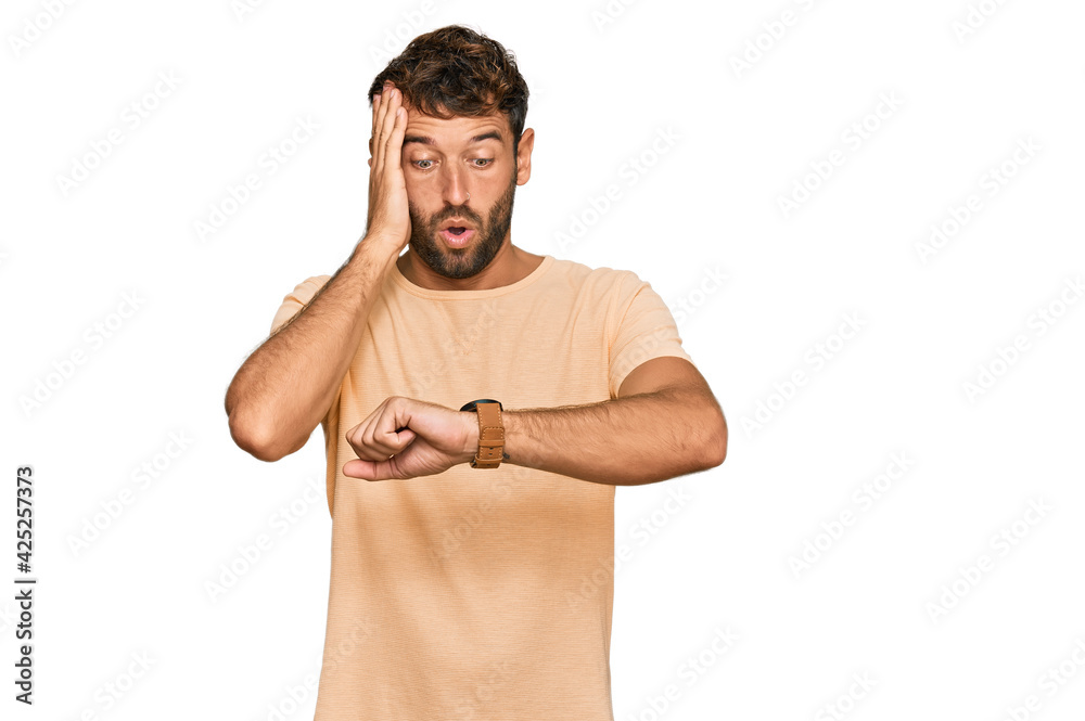 Poster Handsome young man with beard wearing casual tshirt looking at the watch time worried, afraid of getting late