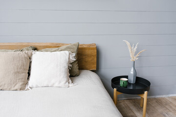 Black modern bedside table next to the double bed with grey bedding in a simple bedroom interior