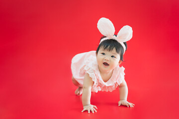 Asian Baby in Easter bunny hairband. Happy baby smiling and crawling on red background. Cute 6 months baby start crawling with copy space as Easter concept, baby or kid department in hospital.