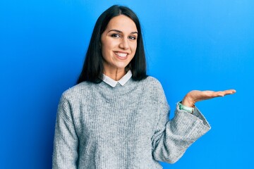 Young hispanic woman wearing casual clothes smiling cheerful presenting and pointing with palm of hand looking at the camera.