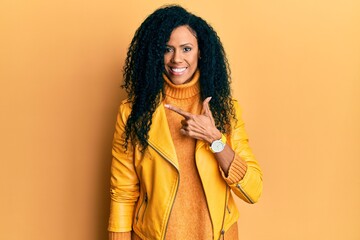 Middle age african american woman wearing wool winter sweater and leather jacket cheerful with a smile on face pointing with hand and finger up to the side with happy and natural expression