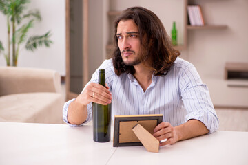 Young man drinking alcohol at home in unhappy love concept