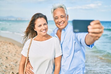 Middle age hispanic couple smiling happy making selfie by the smartphone at the beach.