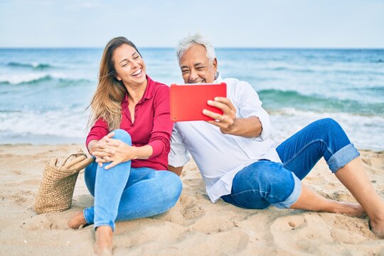 Middle age hispanic couple smiling happy making selfie by the tablet at the beach.