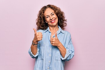 Middle age beautiful woman wearing casual denim shirt standing over pink background Pointing to the back behind with hand and thumbs up, smiling confident