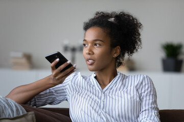 Young biracial woman hold use modern smartphone record audio message on gadget. Millennial African American female talk speak on cellphone call on loudspeaker, activate digital voice assistant.