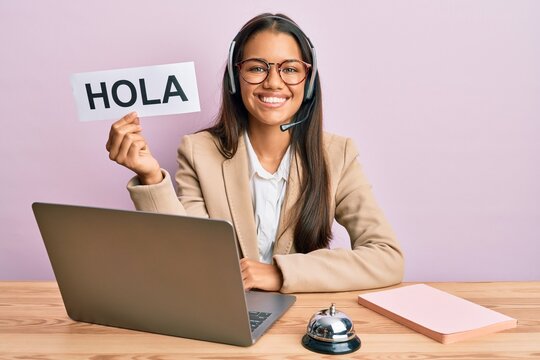 Beautiful hispanic woman wearing operator headset holding hola greenting looking positive and happy standing and smiling with a confident smile showing teeth